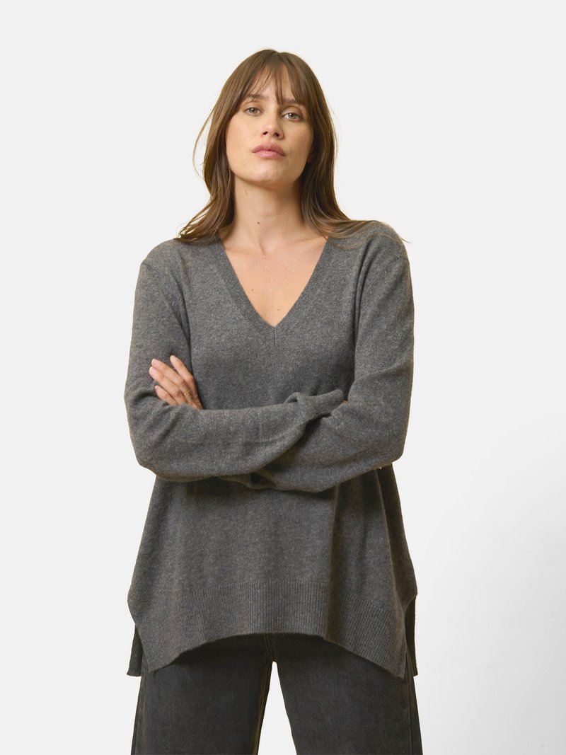Szary, oversize sweter z głębokim dekoltem w serek, wykonany z miękkiego materiału. Posiada długie rękawy, ściągacz u dołu oraz luźny krój z bocznymi rozcięciami.