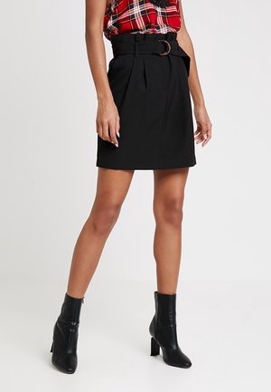 Falda negra hasta la rodilla con detalle de cinturón, pliegues y una textura suave. Combinada con botines negros de tacón y una blusa de cuadros rojos.
