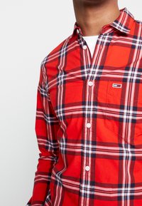 Camicia a quadri rossa in cotone, con bottoni bianchi, taschino sul petto e patch con il logo Thomas. Maniche lunghe con polsini abbottonati.