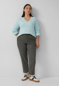 Hellblauer, kabelgestrickter Pullover mit V-Ausschnitt, kombiniert mit dunkelgrauen, schmal zulaufenden Hosen und weißen Sneakern mit schwarzen und braunen Akzenten.