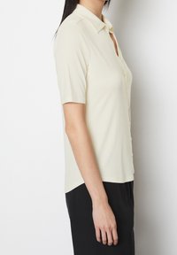 Kortærmet skjorte med knapper i lys gul, lavet af blødt stof. Har en spids krave, slim fit og rundede kant.