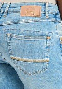 Lichtblauwe denim jeans met een leren label op de taille en twee achterzakken met contrasterende stiksels en gouden accenten.