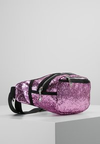 Růžová ledvinka s flitry, vybavená černými kapsami na zip a nastavitelným popruhem. Lesklá textura se stříbrnými kovovými doplňky. Kompaktní obdélníkový tvar.