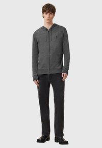 Grå zip-up hoodie i mjukt, andningsbart tyg, med huva, kängurufickor och ribbade manschetter, bärs tillsammans med svarta raka jeans.