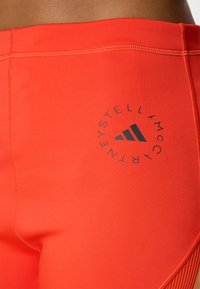Șorturi atletice roșii cu o textură netedă, un talie înaltă și un logo Adidas imprimat închis pe lateral.