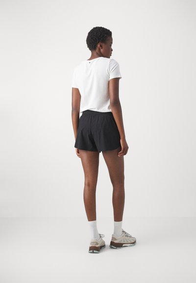 Svarte shorts med elastisk midje kombinert med en hvit t-skjorte med korte ermer. Brukt med lysegrå joggesko og hvite ankelstrømper.