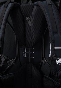 Interior de mochila negra con sistema de ajuste de altura con marcas "L", "M" y "S", acolchado texturizado y hebillas seguras.