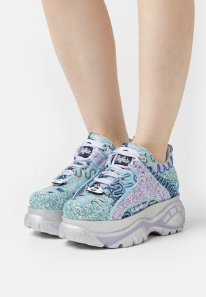 Baskets compensées en matériau bleu et argenté scintillant, présentant des motifs de vagues complexes, des accents pailletés et une semelle épaisse et texturée.