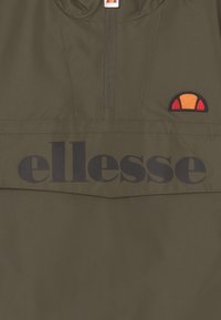 Olijfgroen windjack met een half-zip ontwerp, met een groot zwart "ellesse" logo en een geborduurd oranje en rood logo erboven.