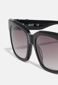 Occhiali da sole neri oversize con lenti sfumate, design della montatura angolare, materiale in plastica liscia e dettaglio del logo sulla stecca.