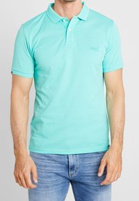 Polo shirt bleu clair en coton doux avec un col, des manches courtes et un logo discret sur la poitrine. Convient pour un usage décontracté.
