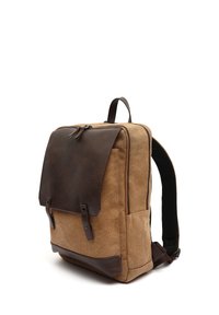 Mochila de lona marrón con solapa de cuero marrón oscuro, cierre de cremallera, correas de tela, bolsillos laterales y detalles de botón. Forma rectangular.