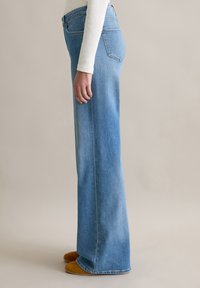 Hellblaue, ausgestellte Jeans aus Denim mit hoher Taille, die ein klassisches Fünf-Taschen-Design und sichtbare Nähte entlang der Seitennähte aufweist.
