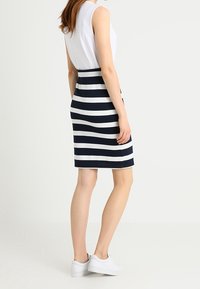 Námořnická modrá a bílá pruhovaná sukně, přiléhavý střih, délka ke kolenům, vyrobená z elastické tkaniny. Kombinována s bílým tílkem bez rukávů a bílými teniskami.