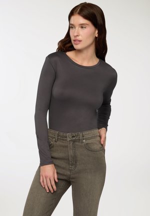 Body a maniche lunghe di colore grigio scuro in un tessuto liscio e elasticizzato. Abbinato a jeans in denim verde oliva a vita alta con tasche frontali.