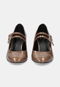 Zapatos de charol marrón con punta redonda, dos cintas finas con una hebilla decorativa, acabado brillante y un tacón bajo.