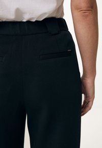 Pantalones negros ajustados con una textura suave, con una cinturilla y dos bolsillos traseros. El diseño es recto con detalles minimalistas.