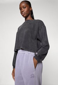 Gray cropped sweatshirt made of cotton with loose sleeves, featuring a logo detail. Paired with light gray sweatpants, both casual styles.