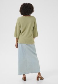 Hellgrünes Strickoberteil mit ¾-Ärmeln, kombiniert mit einem hellblauen Denim-Maxiskirt und braunen Blockabsatzsandalen.