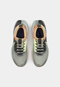 Baskets de sport grises avec un dessus texturé, des accents noirs et orange, des lacets vert lime et un design de semelle incurvée. Marque Nike visible.