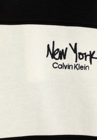 Tessuto di cotone bianco e nero con righe orizzontali. Ricamato "New York" in corsivo nero e "Calvin Klein" sotto in carattere più piccolo.