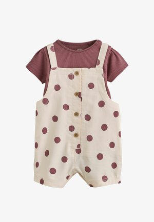 T-shirt mauve côtelé à manches courtes avec une salopette courte crème ornée de pois mauves et des boutons en bois à l'avant.