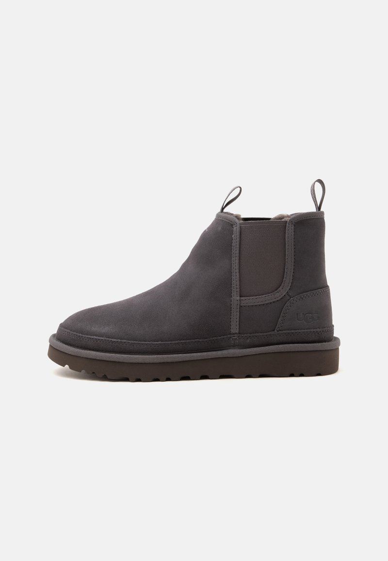 Bottine en daim gris foncé avec languettes pour faciliter l’enfilage, panneaux latéraux élastiques et semelle plate en caoutchouc marquée du logo UGG au talon.