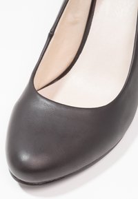Chaussure en cuir noir avec un bout arrondi, texture lisse et un design découpé sur les côtés, mettant en valeur une doublure intérieure pâle.