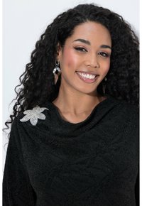 Černá košile s texturovaným listovým vzorem a stříbrnou květinovou sponou na rameni. Modelka má na sobě geometrické stříbrné náušnice.