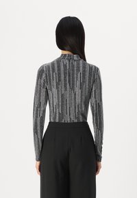 Langærmet, tætsiddende top i et sort og sølvstribet mønster, med en mock neck og blødt, tekstureret stof. Sammen med skræddersyede sorte bukser.