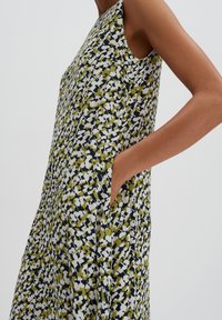 Ärmelloses Kleid mit Blumenmuster in einer Kombination aus Grün, Marineblau und Weiß, mit seitlichen Taschen und einem fließenden Schnitt.