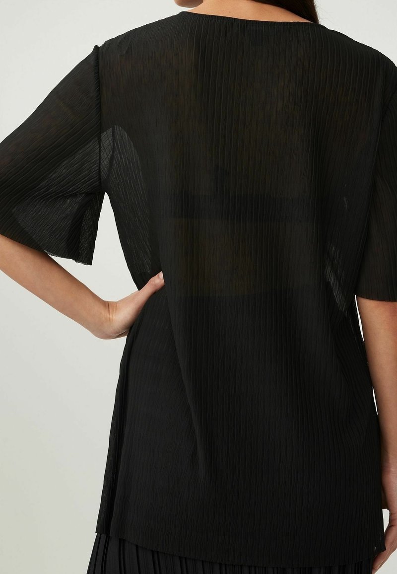 Blusa nera plissettata con maniche corte, tessuto leggero e vestibilità rilassata. Texture notevole con strisce verticali e scollatura arrotondata.