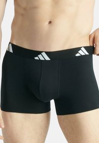 Czarne bokserki wykonane z elastycznego materiału z szerokim czarnym pasem w talii z białymi akcentami logo Adidas oraz smukłym, dopasowanym krojem.