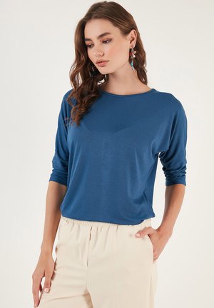 Blue lightweight top with long sleeves and a crew neckline, paired with beige trousers. Smooth fabric, relaxed fit, and simple design.
