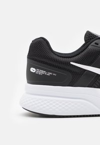 Baskets de course noires avec tige en maille, swoosh Nike blanc, semelle blanche rembourrée, détails texturés noirs et marquage visible à l'arrière.
