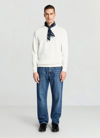 Sweat-shirt blanc à manches longues, associé à un jean bleu ample et une écharpe marine nouée autour du cou. Des chaussures noires complètent la tenue.