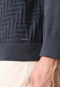 Grijze gebreide pullover met textuur, voorzien van een geometrisch patroon, geribde manchetten en zoom, met een zwart label met de tekst "AUTOGRAPH."