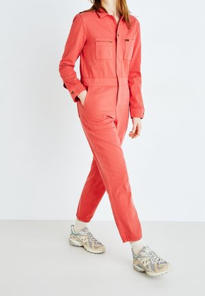 Rød bomuldsheldragt med lange ærmer, to brystlommer og afsmalnende ben. Båret med lysegrå og beige sneakers.