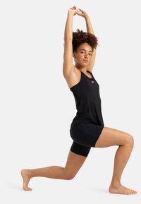 Musta urheilullinen toppi ja shortsit, suunniteltu liikkumiseen, istuvassa tyylissä. Kangas vaikuttaa kevyeltä ja joustavalta, ja siinä on minimaalisesti brändäystä.