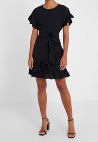 Svart klänning med korta ärmar, ruffled detaljer, bälte i midjan och lager av ruffled nederkant. Tillverkad av strukturerad tyg.