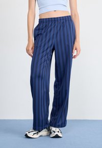 Pantalons large bleu marine avec des rayures verticales bleues, dotés d'une taille élastique. Portés avec des baskets blanches et noires.