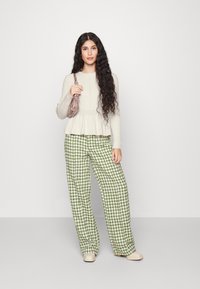 Haut en peplum crème à manches longues et pantalon large en vichy vert. Des chaussures claires et un petit sac à motif complètent la tenue.