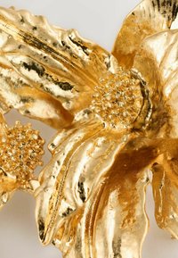 Goldfarbener Blumenbrosche mit strukturierten Blütenblättern und einem zentralen Cluster von Perlen, das das filigrane Design und die reflektierenden Oberflächen betont.