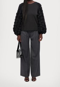 Haut noir avec des manches bouffantes texturées à fleurs, associé à un pantalon large gris. Les accessoires comprennent un petit sac à main noir et des sandales à lanières.