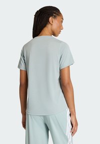 Žena s vrkočmi, ktorá má na sebe svetlomodrú krátkos rukávovú košeľu a svetlomodré nohavice s bielymi bočnými pruhmi, stojaca chrbtom ku kamere.