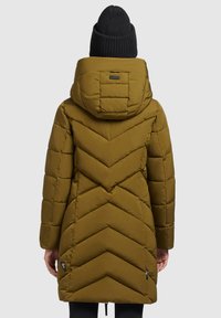 Giacca puffer verde oliva con cuciture a zig-zag e cappuccio. Presenta un dettaglio a zip nelle cuciture e un berretto a coste indossato sulla testa.