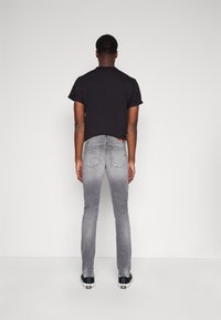 Camisa negra de manga corta con dobladillo curvado, combinada con jeans ajustados grises que presentan un lavado en degradado y bolsillos traseros. Zapatillas negras visibles.