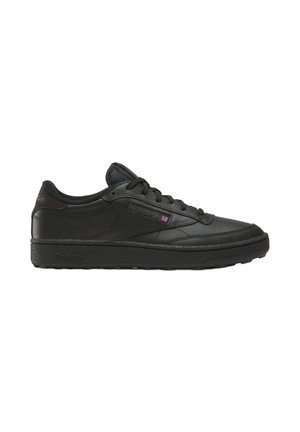 Zapatilla negra de piel de caña baja con cordones y suela texturizada, con el logo sutil de Reebok y una pequeña bandera del Reino Unido en el lateral.