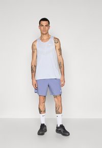 Débardeur gris clair avec un motif texturé, associé à un short bleu. Chaussures de sport noires et chaussettes blanches avec un logo noir.