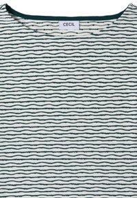 Gros plan d'un tissu blanc avec des rayures horizontales vert foncé irrégulières et une étiquette de marque « CECIL » au niveau de l'encolure.